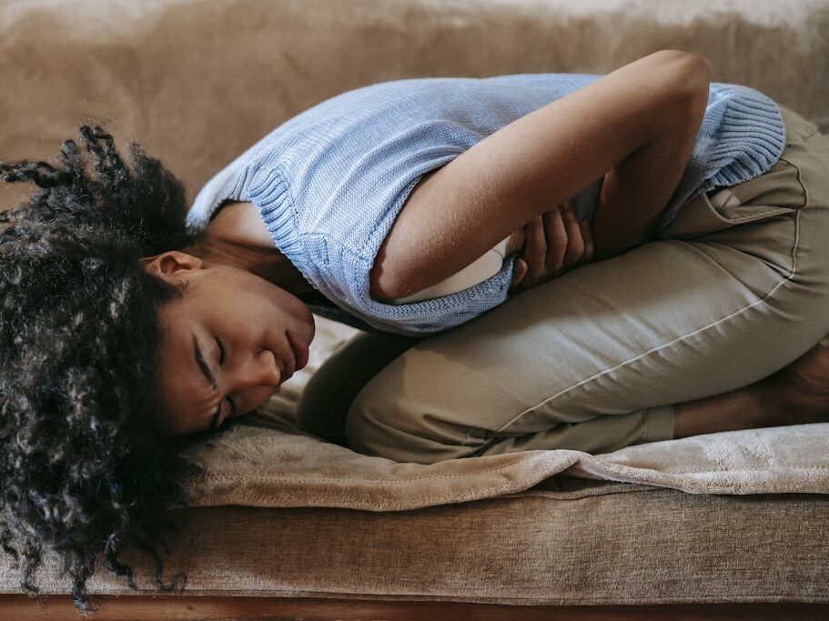 Side view of young African American female in agony on couch while having pain in stomach